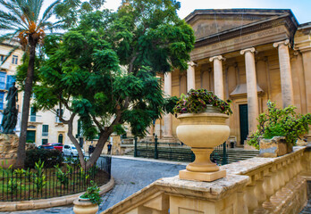Obraz premium Stone vase with green plants, St Paul s Pro-Cathedral in the background, Independence Square, Valletta, Malta