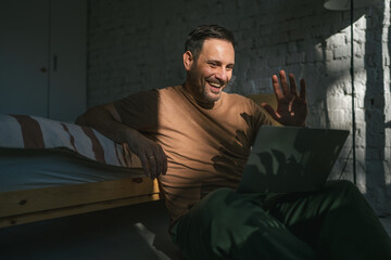 Fototapeta premium Man video calling smiling and waving enjoying remote connection