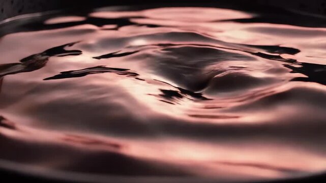 Slow motion of rose copper liquid ripples on a charcoal black background, metallic shimmer, mesmerizing fluid dynamics.