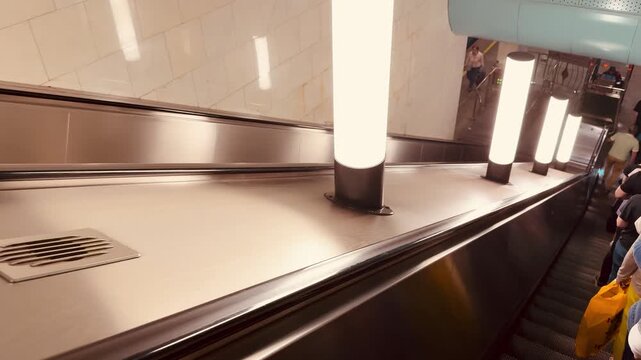 Empty metro escalator with stainless handrail descending view captures quiet underground station fluorescent lighting casts soft reflections on polished metal surfaces subtle motion blur