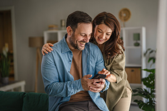 Couple using smart phone together at home, connecting online