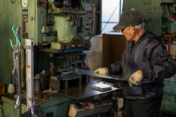Senior Japanese factory worker operating metal press machine in small manufacturing workshop