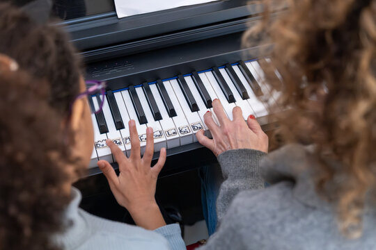 Teacher and student hands playing piano keys with notes labeled, focusing on music education and skill development