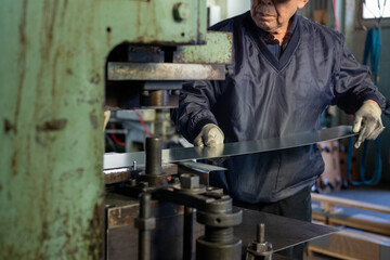 Experienced Japanese factory worker feeding steel sheet into metal press machine at small manufacturing workshop