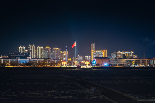 Chinese flag flying above illuminated buildings in Heihe. View from across the Amur River at night.