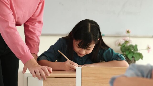 Asian girl writing or taking a note while teacher checking classwork. Caucasian teacher help happy student doing test or classwork while diverse student study in science lesson. Education. Pedagogy.