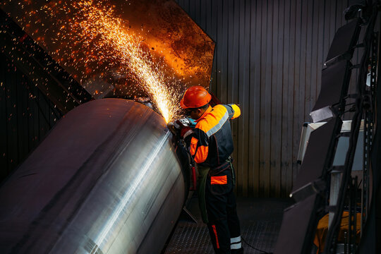 Pipe factory production. Male worker grinding butt weld pipe