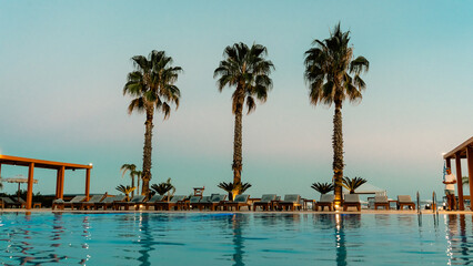 Beautiful ocean view at Faliraki beach, Rhodes, with pebble shore, distant people, and colorful umbrellas under a stunning summer sunset. Serene, picturesque Greek island scene.