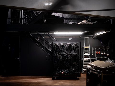 Wide view of theatre backstage area with cable racks, metal stairs, ladder, power sockets and flight cases