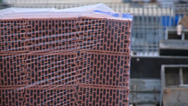 Construction Site with Stack of Red Clay Cinderblock Hollow Bricks Wrapped in Plastic Packaging Waterproof Foil