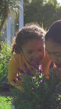 Vertical video: Mom guiding girl in orange top, touching and sniffing lavender and learning in yard