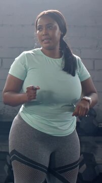 Vertical video: Tapping smartwatch, woman leading warm-up in gym with dumbbells, wearing mint top