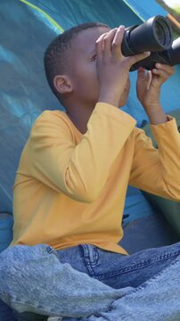 Vertical video: Seeing outside kid yellow tee lifting binoculars scanning lowering smiling in tent