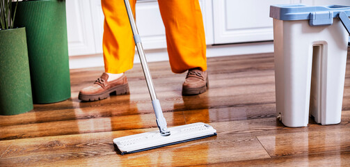 Professional cleaner washes wooden laminate floor. Woman in orange pants cleans house interior....