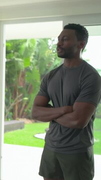 Vertical video: Hearing off-camera call, man in sportswear replying by glass doors, backyard plants