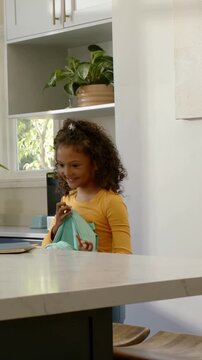 Vertical video: Smiling girl in yellow packing blue folder into mint backpack at home for school