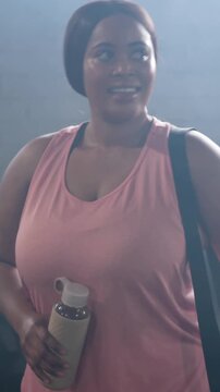 Vertical video: Starting workout in gym, walking woman in pink, tapping smartwatch, holding bottle