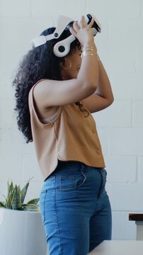Vertical video: Placing woman in tan top and jeans adjusting white VR headset at office, testing