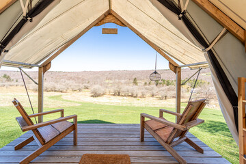 Luxury glamping tent interior with wooden chairs and panoramic countryside view on a sunny day