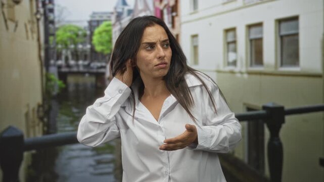 Woman checks her palm while holding hand to ear on canal street in amsterdam; concern uncertainty self reflection.