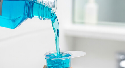 Vibrant blue mouthwash pouring into a measuring cup for oral care
