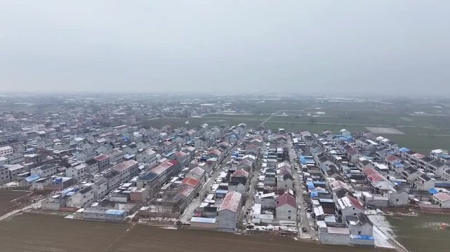 SHANDONG, CHINA - JANUARY 27 2026: An aerial drone perspective captures the organized rows of modern residential houses in a rural village covered in a light dusting of winter snow. The footage illust