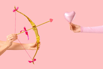Naklejka premium Female hands with cupid's bow and heart shaped balloon on pink background. Valentine's Day celebration