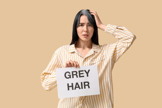 Young woman holding paper with text GREY HAIR on beige background