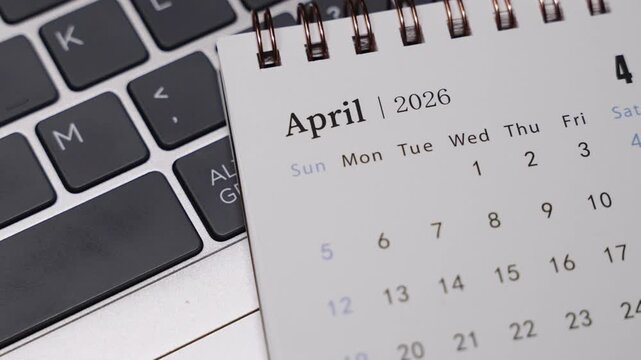 Close-up of a desk calendar with April 2026 visible on a laptop keyboard. Slow rightward camera rotation presents clear date structure and structured monthly planning concept indoors.
