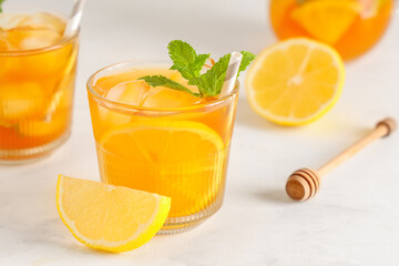 Naklejka premium Glass of fruit tea with lemon, mint leaves and wooden dipper on light background