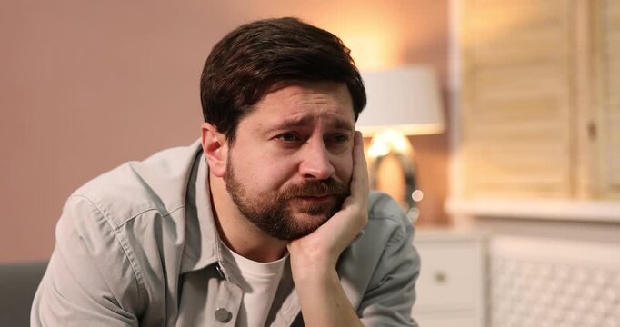 Unhappy man feeling fatigue on sofa at home. Camera moving right