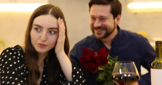 Bad date. Embarrassed woman ignoring flirting man with roses at table during dinner indoors. Camera moving forward