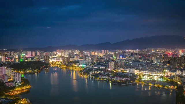 Nighttime aerial time-lapse of Nanhu Lake in Jiujiang, glowing city lights, serene lake reflections, and urban skyline under a dark sky. Jiangxi Province, China.