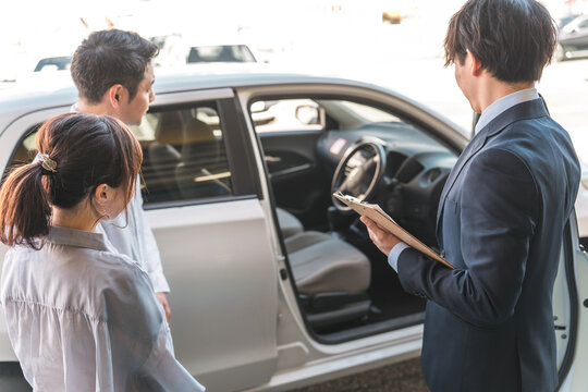 A young Asian male salesman serving a couple who came to buy, appraise and purchase a car