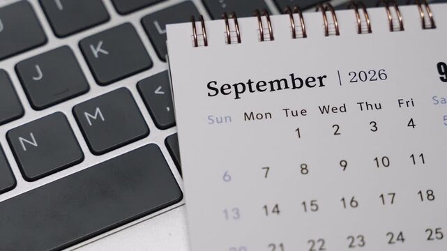 Close-up of a desk calendar showing September 2026 placed next to a laptop keyboard. Camera slowly rotates to the right, revealing clear date layout and calm monthly planning concept in a modern work