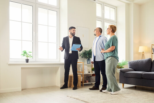 Realtor and agent guide a senior couple through new apartment during a tour and viewing, helping buyers assess the interior and showing key home features. Real estate market and buying property.