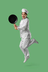 Naklejka premium Beautiful young happy Asian chef in uniform with frying pan jumping on green background
