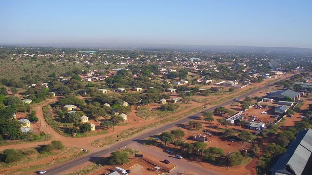 aerial drone view captures a developing mixed-use area in Molepolole, Botswana, featuring warehouse buildings and residential homes in a dry African landscape with no people visible
