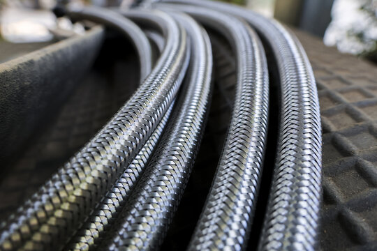 Detailed close up of braided metal hose and stainless steel pipe in an industrial factory setting. flexible tube has durable wire and strong metallic texture
