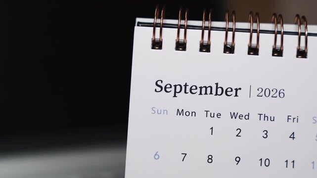 Close-up of a desk calendar on a laptop keyboard as a finger points to a date in September 2026. Static camera highlights clear date indication and organized monthly planning concept in a modern offi