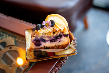 A beautiful blueberry cheesecake topped with lemonade is served on a plate, with a cafe as the backdrop.