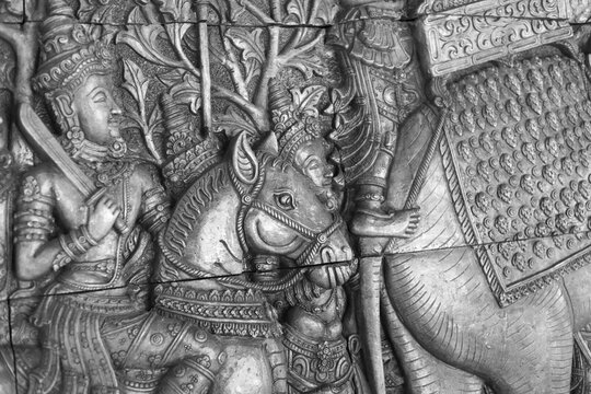 Ancient stone carving detail of Khmer bas relief sculpture on temple wall. Black and white artwork showing historic warrior on horse with sword in battle
