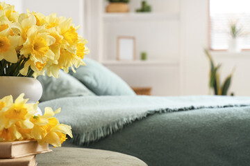 Vase with daffodils and books on green pouf in bedroom, closeup