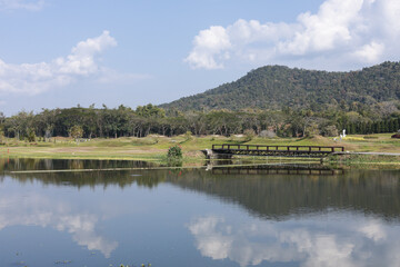 Obraz premium Peaceful landscape with beautiful lake and mountain view. wooden bridge crosses water with forest in background under blue sky, perfect reflection