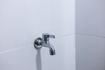 Clean chrome water tap and faucet on white tile wall in modern bathroom. simple, minimalist,...