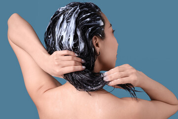 Asian woman applying hair mask on blue background, back view