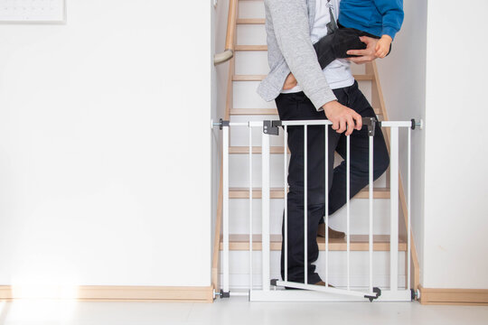 子どもを抱いてベビーゲートを開ける親