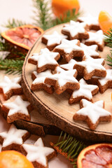 Fototapeta premium Wooden board of star-shaped gingerbread cookies with mandarin, dried orange and fir branches on beige background