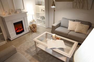 Obraz premium Interior of elegant living room with grey sofas, fireplace, white furniture and glowing lamps at evening