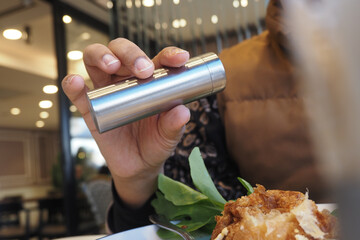Person uses pepper shaker at restaurant during lunch